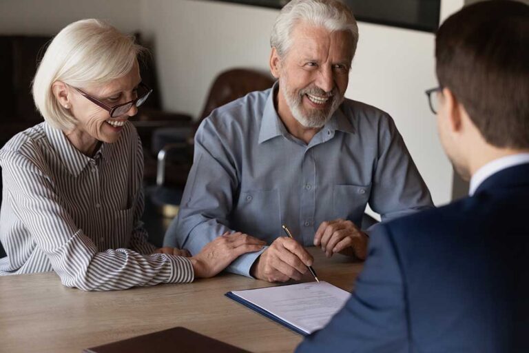 Two young parents review estate planning documents at a kitchen table while their children play nearby.